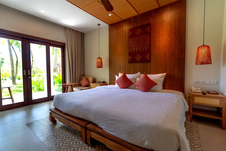 Lit king size face aux portes-fenêtres ouvertes sur le jardin tropical